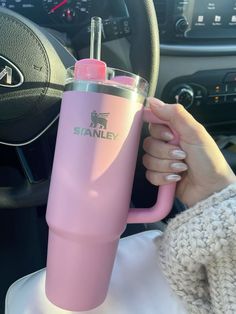 a woman is holding a pink cup in her hand while she sits behind the steering wheel