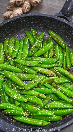 green beans in a frying pan with sesame seeds and garlic flakes on the side