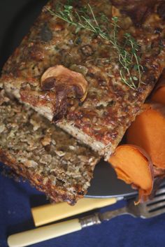 a piece of meatloaf with carrots and mushrooms on a plate next to a fork