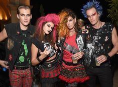 four people dressed up in punk clothing posing for a photo with one holding a drink