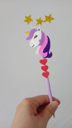 a hand holding a pink and purple unicorn wand with stars on it's head