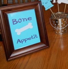 a wooden table topped with two framed pictures next to a vase filled with dirt and bone appetizers