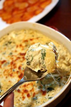 a person holding a spoon full of cheese and broccoli casserole on a table