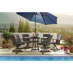 an outdoor table with chairs and umbrella next to a swimming pool