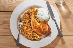 a white plate topped with chicken, rice and mashed potatoes next to a glass of water