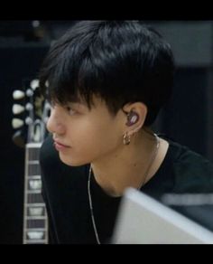 a young man with ear piercings sitting in front of a guitar