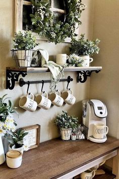 some plants and coffee cups are on a table in front of a wall mounted shelf