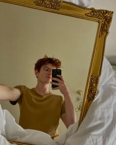 a man taking a selfie in front of a mirror with white sheets on the bed