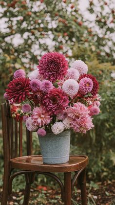 a bucket filled with lots of flowers sitting on top of a wooden chair in front of trees