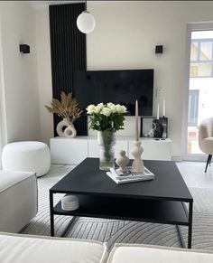 a living room with white furniture and flowers on the coffee table in front of a flat screen tv