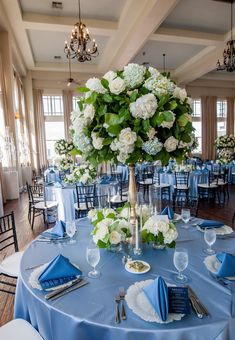 a blue table cloth with white flowers and greenery is set up for a formal function