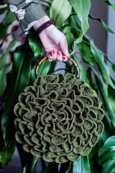 a woman's hand holding a green purse over a plant with leaves in the background