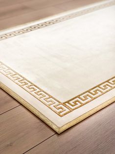 a white rug with gold border on top of a wooden floor in an empty room