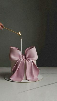 a person lighting a candle on top of a pink bow shaped cake with a stick