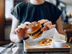 a person sitting at a table eating a hamburger and french fries