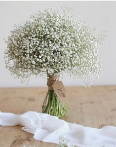 a bouquet of baby's breath sitting on top of a wooden table next to a white cloth