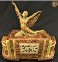 a gold and green clock with a woman sitting on it's back holding her arms in the air