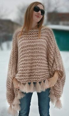 a woman standing in the snow wearing a sweater with fringes on it's sleeves