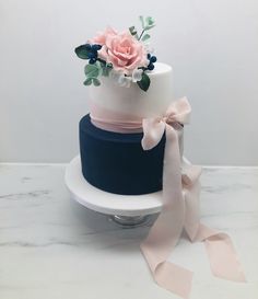 a three tiered cake with pink and blue flowers on top, sitting on a marble table