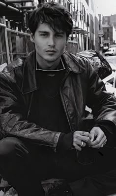 black and white photograph of a man sitting on a bench in an alleyway wearing a leather jacket