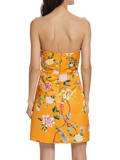 a woman in an orange floral dress with her back turned to the camera, looking down