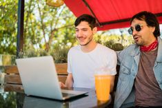 two young men sitting at a table with a laptop and orange juice in front of them