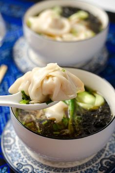 two bowls filled with dumplings and broccoli on top of a blue table