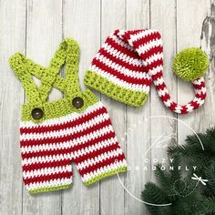 two crocheted christmas outfits and a hat on a wooden surface with pine branches