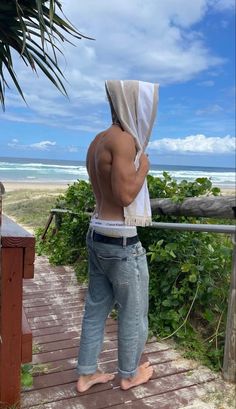 a man standing on a wooden walkway next to the ocean holding a towel over his head