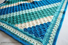 a crocheted blanket is laying on top of a white bed sheet with blue and green stripes