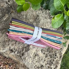 a bunch of different colored papers sitting on top of a rock next to some leaves