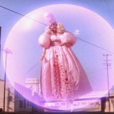 a woman in a pink dress and hat standing next to a giant bubble with her hands on her hips