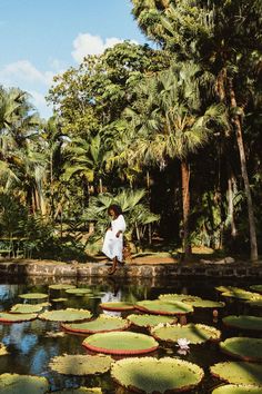 a woman standing on the edge of a body of water surrounded by lily pads and palm trees