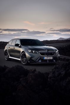 the front end of a silver car on a road with mountains in the back ground