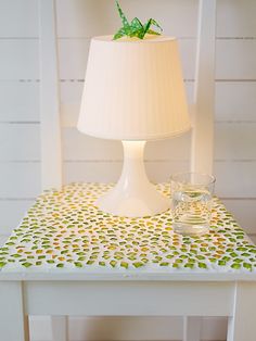 a white table with a lamp on top of it and a glass cup next to it