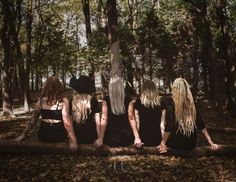 four women sitting on a log in the woods with their backs turned to the camera