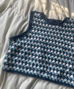 a blue and white crocheted sweater laying on top of a bed next to a pillow