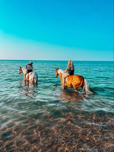 three people riding horses in the ocean on a sunny day with clear blue skies above