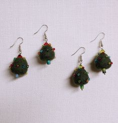 three green earrings with beads hanging from them on a white tablecloth surface, one is wearing a pair of silver ear wires and the other two are decorated with colorful beads