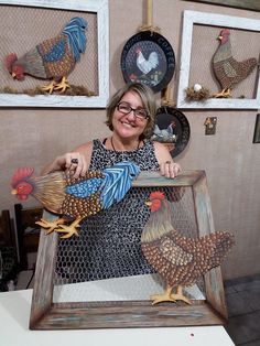 a woman is holding up some fake chickens in front of two pictures on the wall