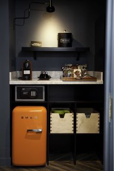 an orange refrigerator sitting in the corner of a room next to a shelf with items on it