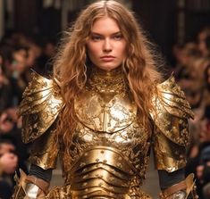 a woman with long hair and gold armor on the catwalk at a fashion show