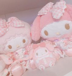 two hello kitty stuffed animals sitting next to each other on a shelf with pink bows