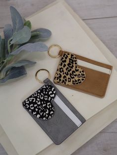 two keychains with leopard print on them sitting next to a plant and a card holder