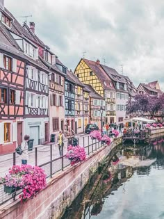 people are walking along the river in an old european town with flowers growing on it