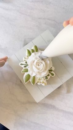 someone is decorating a white flower with green leaves