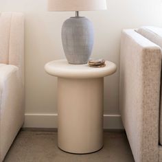 a table with a lamp on it next to two couches and a white chair