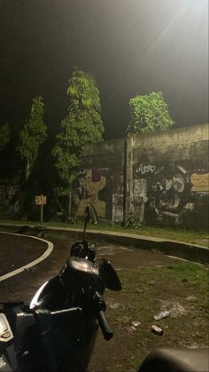 a motorcycle parked in front of a wall with graffiti on it's walls and trees