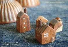 three small clay houses sitting on top of a blue carpet next to two vases