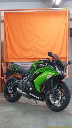 a green and black motorcycle parked in front of an orange wall with curtains behind it